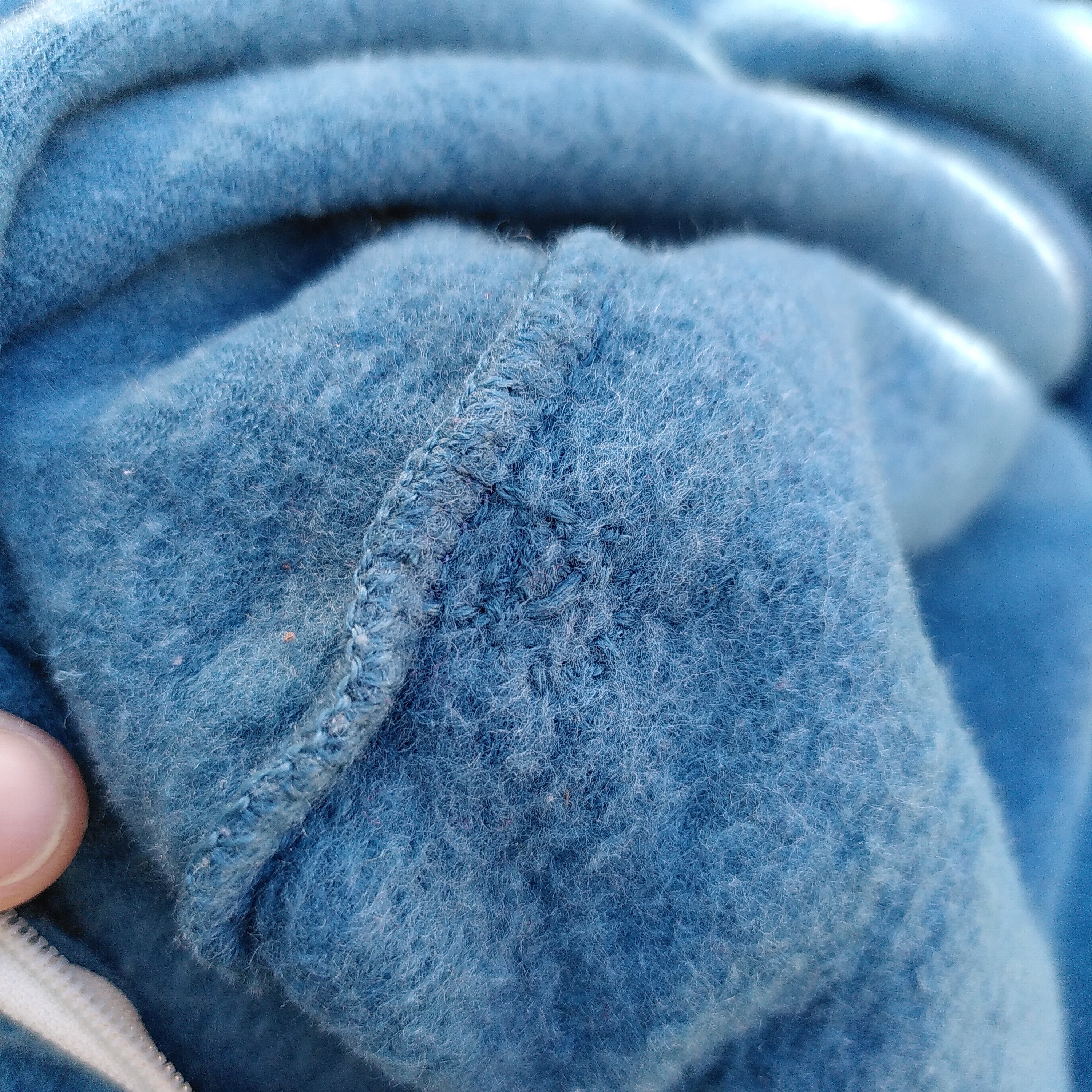 Mit hellblauem Garn kaum sichtbar verschlossenes Loch in einem hellblauen Wollfleeceschlafsack.