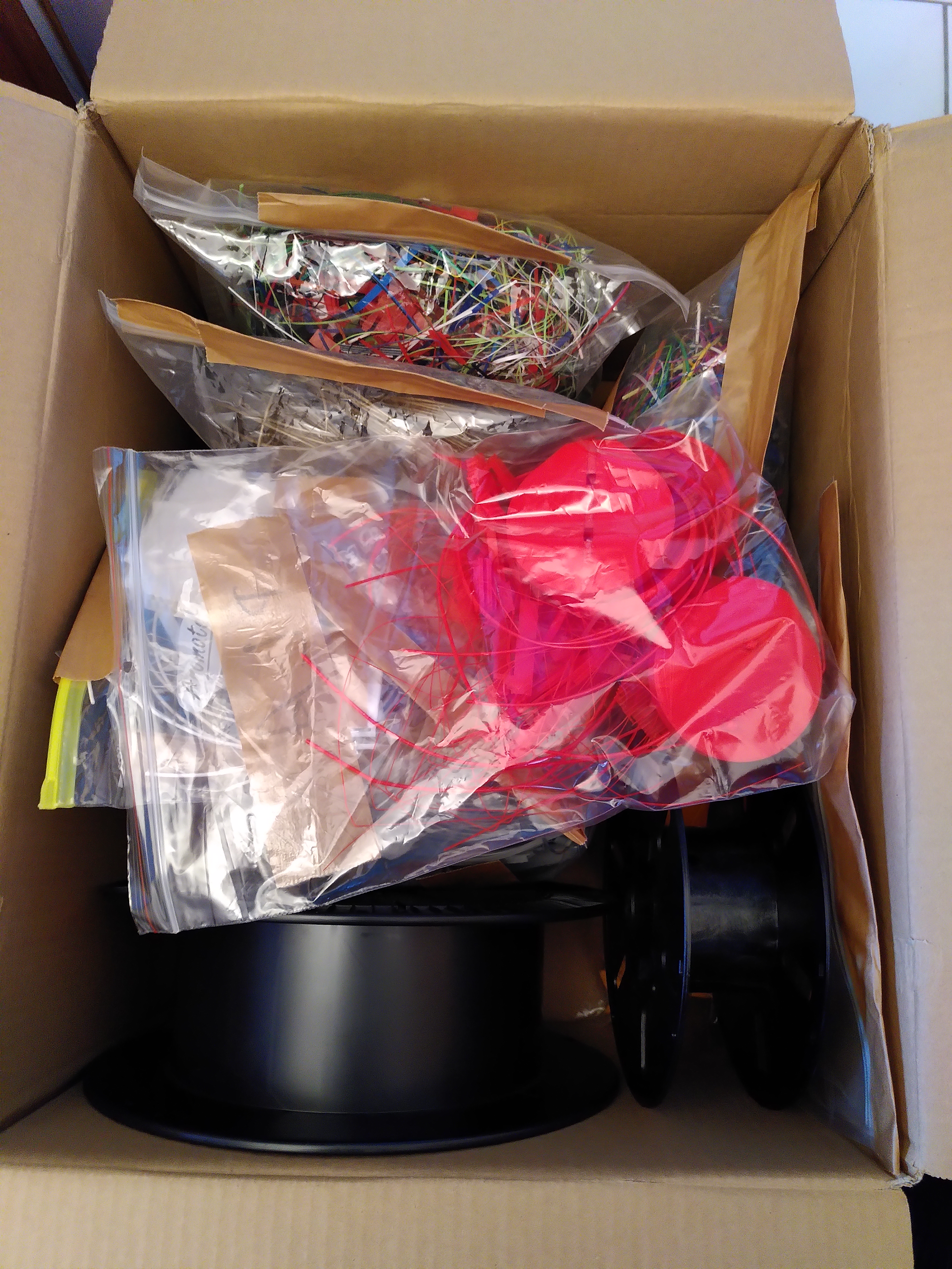 Ein Karton voll gepackt mit Tüten voller 3D Druckreste und 2 leeren Spulen